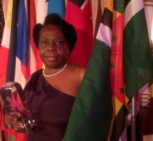 Jean Joseph poses next to the flag of Dominica with her award