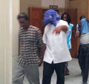 Degallerie (head covered) being led out of court after sentencing 